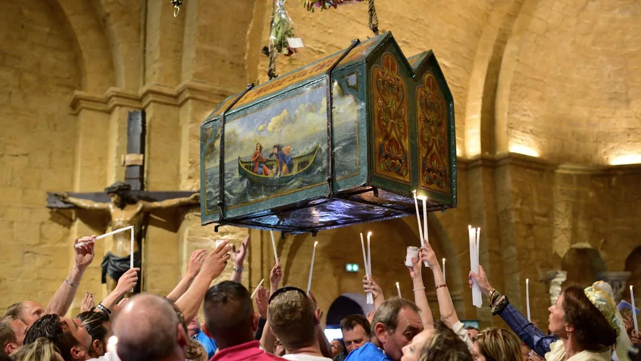 A painted reliquary chest carried above a crowd holding candles inside a stone church.